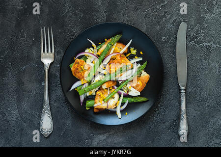 Salat mit gebratener Halloumi, Spargel und Orangenschale. Ansicht von oben mit Besteck. Dunkle konkreten Hintergrund Stockfoto