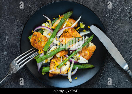 Salat mit gebratener Halloumi, Spargel und Orangenschale. Ansicht von oben mit Besteck. Dunkle konkreten Hintergrund Stockfoto