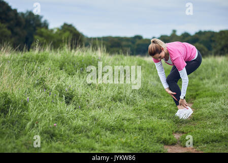 Eine Ausübung der Frau in Passform Verschleiß beim Laufen im Freien, Stop, um die Kupplung einen verletzten Knöchel. Stockfoto