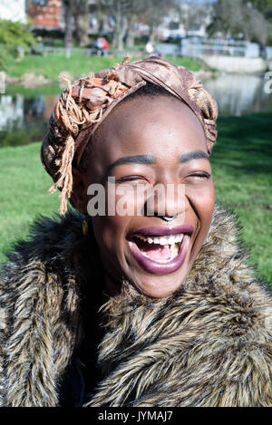 Junge schwarze Frau das Tragen von Kleidung und mit Make-up und eine Nase piercing lacht bei Tageslicht Stockfoto