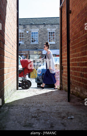 Frau Schieben eines Kinderwagens und halten ein Kind in der Hand zu Fuß auf einem hohen-Straße während des Tages in England Stockfoto