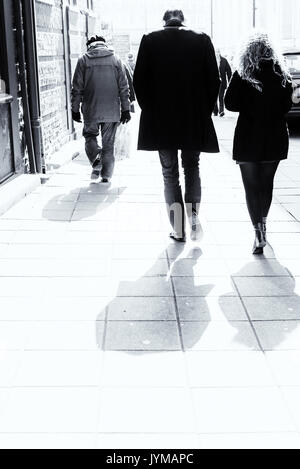 Mann und Frau gekleidet in Smart schwarze Kleidung zu Fuß eine hell Street in rauen stark überbelichtet Sonnenlicht beleuchtet Stockfoto