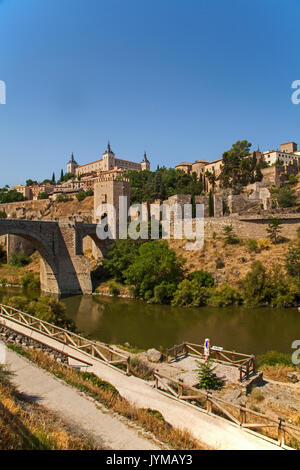 Frau mit Blick auf die Stadtmauern von Toledo Spanien über den Fluss Tejo mit Alcantara Bridge und dem Alcazar im Hintergrund Stockfoto