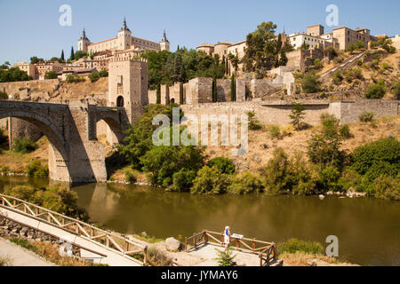 Frau mit Blick auf die Stadtmauern von Toledo Spanien über den Fluss Tejo mit Alcantara Bridge und dem Alcazar im Hintergrund Stockfoto