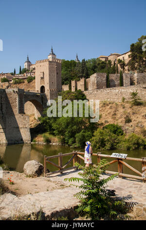 Frau mit Blick auf die Stadtmauern von Toledo Spanien über den Fluss Tejo mit Alcantara Bridge und dem Alcazar im Hintergrund Stockfoto