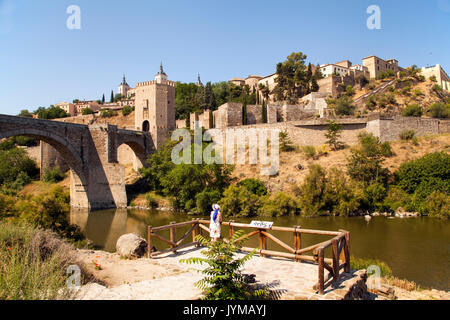 Frau mit Blick auf die Stadtmauern von Toledo Spanien über den Fluss Tejo mit Alcantara Bridge und dem Alcazar im Hintergrund Stockfoto