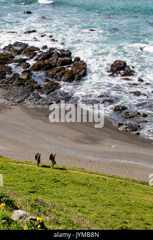 Der Mann und die Frau zu Fuß Coastal Trail wie Wellen auf die Felsen Stockfoto