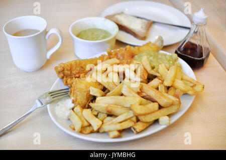 Eine Platte der traditionellen britischen Fish und Chips, mit Erbsenpüree, Brot und Butter, Essig, Tartar Sauce, und eine Tasse Kaffee. Stockfoto