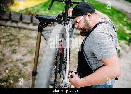 Schlosser arbeitet mit Fahrrad Rad, cycle Workshop Outdoor. Bärtige Fahrradmechaniker in Schürze Stockfoto
