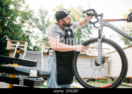 Professionellen Fahrradmechaniker in Schürze passt Bike. Zyklus Workshop Outdoor. Radfahren Sport, bärtigen service Mensch arbeiten mit Rad Stockfoto