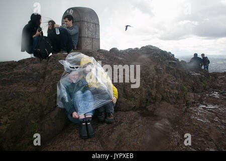 Touristen gefangen in einer Windböe Regenschutz suchen auf der Oberseite von König Arthur's Seat. Der Gipfel des König Arthur's Seat ist ein beliebtes Ziel für beide Stockfoto