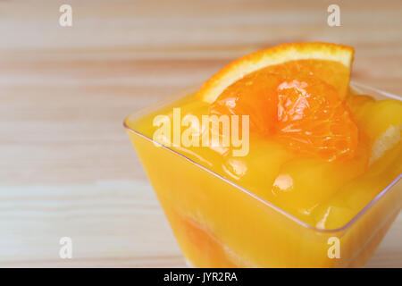 Geschlossen bis eine lebendige Farbe Mandarin orange Kuchen mit frischen Orange in Glasschale auf hölzernen Tisch lagen Stockfoto