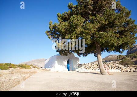 Agios Joanne, eine kleine Kirche auf der Insel Tilos, Dodekanes, Griechenland über dem Hafen von Livadia, um verlassene Gera im Schatten unter der großen Kiefer. Stockfoto