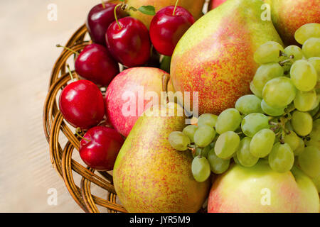 Obst ernten. Organische frische Äpfel, Birnen, Trauben und Pflaumen in einer gewebten Holzplatte Stockfoto