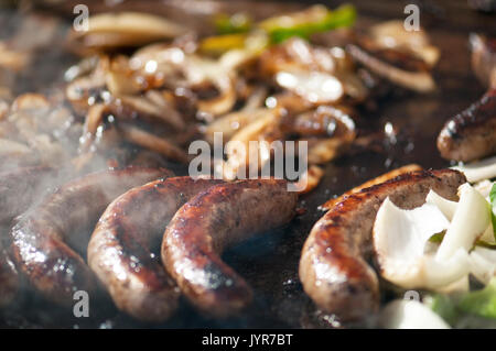 Gegrillte Bratwürste, grüne Paprika und Onons auf dem Grill, die durch Rauch umgeben mit Fokus auf Center Gören. Stockfoto