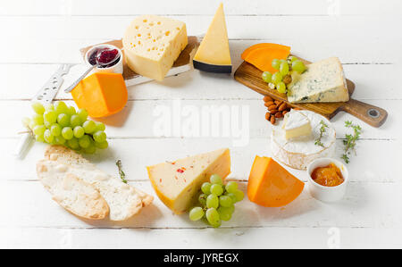 Verschiedene Arten von Käse serviert mit Trauben, Marmelade, Brot und Muttern auf hölzernen Hintergrund Stockfoto