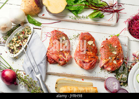 Marinierte Schweinesteaks auf Schneidebrett und frisches Gemüse für eine gesunde Ernährung. Stockfoto