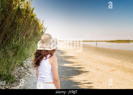 Zurück Blick auf kurvigen reife Frau in sehr guter Form mit breiten Hut auf einem Sun split Strand Stockfoto