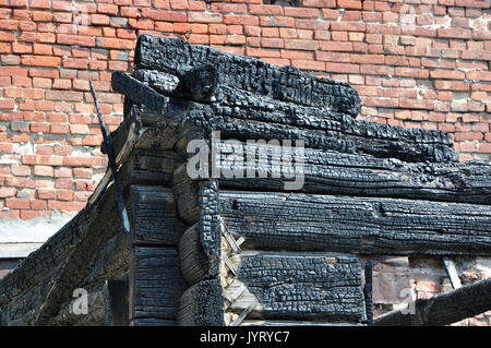 Nahaufnahme eines charry Ecke eines verbrannten Holz- Haus gegen eine Rote Wand. Stockfoto