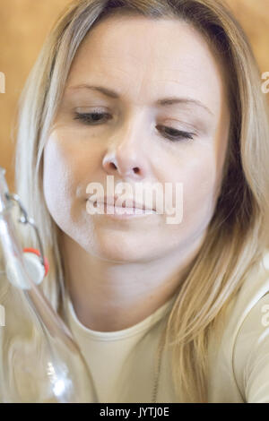 Junge blonde Frau im Vintage Flasche Wasser suchen. Close up candid Portrait. Vertikale crop Stockfoto