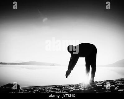 Tiefes Atmen runner Silhouette mit den Händen auf die Knie gebeugt. Seitenansicht zu Sport aktiven Mann stretching Muskeln und Bewegung am Meer Strand. Sun spiegeln Stockfoto