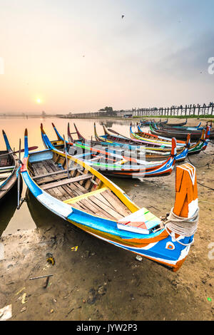 Amarapura, Mandalay, Myanmar. Bunte Boote am Ufer des Taungthaman See bei Sonnenaufgang, mit der U-Bein Bridge im Hintergrund. Stockfoto