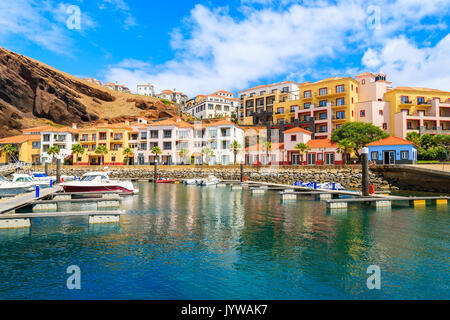 Boote in der Marina mit bunten Häusern in der Nähe von Canical Stadt an der Küste der Insel Madeira, Portugal Stockfoto