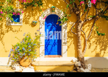 Blaue Tür von einem gelben griechischen Haus mit Blumen dekoriert, Assos, Kefalonia, Griechenland Stockfoto