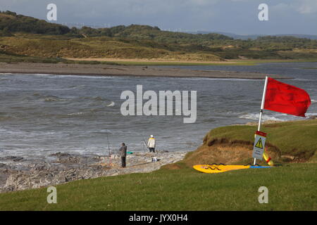 2 Angler warten geduldig auf ein 'Biss' beim Fischen in der Gezeiten- Wasser des Flusses Ogmore an einem klaren sonnigen widny Tag. Stockfoto