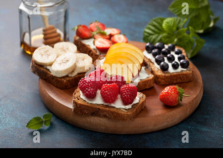 Diät Frühstück. Toast mit Frischkäse und frischen Beeren und Früchte: Bananen, Himbeere, Heidelbeere, Erdbeere, Pfirsich. Stockfoto