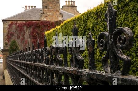 Schrägansicht entlang verzierten viktorianischen Geländer, High Street, Aberlady, East Lothian, Schottland, Großbritannien, mit Steinmauer in rot Efeu bedeckt Stockfoto