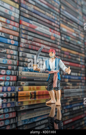Schwert schwingt Spielzeug Pirat stand vor der Stapel von DVDs (Digital Versatile Disc) - Metapher Softwarepiraterie, Chinesisch gefälschte Waren, IP-Diebstahl Stockfoto