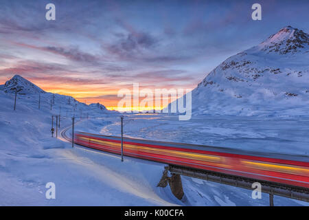 Der Bernina Express geht an den Ufern des Lago Bianco komplett eingefroren, bevor die Sonne aufgeht. Kanton Graubünden. Engadin. Die Schweiz. Europa Stockfoto