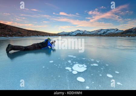 Fotograf in Aktion auf der gefrorenen Oberfläche des Andossi-Sees bei Sonnenaufgang Spluga Tal Valtellina Lombardei Italien Europa Stockfoto