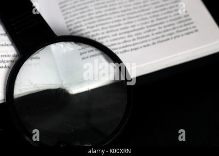 Lupe oben auf ein offenes Buch auf einem Schwarz reflektierende Oberfläche aus Glas Stockfoto