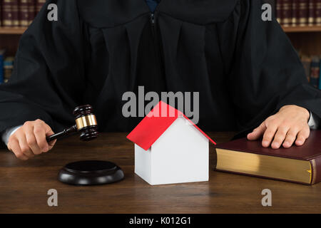 Mittelteil des Richters mit Haus Modell schlagen Hammer am Schreibtisch im Gerichtssaal Stockfoto