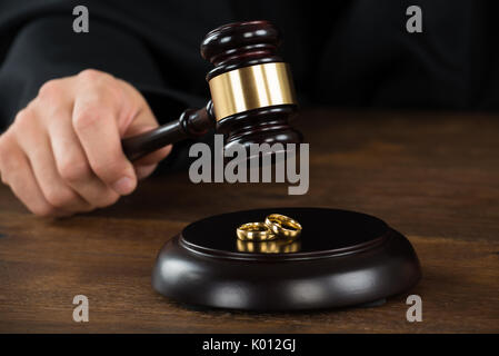 Zugeschnittenes Bild der scheidungsrichter schlagen Hammer auf goldenen Ringe am Schreibtisch im Gerichtssaal Stockfoto
