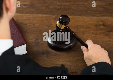 Hohe Betrachtungswinkel der männlichen Richter schlagen Mallet am Schreibtisch im Gerichtssaal Stockfoto