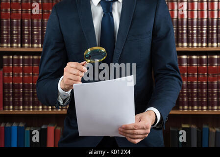 Mittelteil der männlichen Rechtsanwalt prüft rechtliche Dokumente mit Lupe im Gerichtssaal Stockfoto