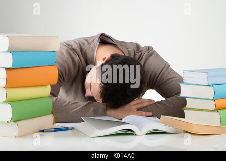 Müde männliche Kursteilnehmer lehnen auf Schreibtisch während des Studiums vor weißem Hintergrund Stockfoto