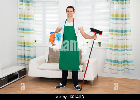 Volle Länge Portrait von glücklichen Menschen in der grünen Schürze holding Reinigung Ausrüstung zu Hause Stockfoto