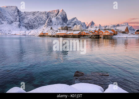 Die Farben der Morgenröte rahmt die Fischerhäuser, umgeben von schneebedeckten Gipfeln Sakrisøy Reine Nordland Lofoten Inseln Norwegen Europa Stockfoto