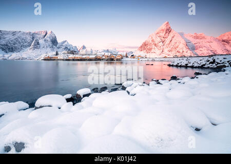 Die Farben der Morgenröte rahmt die Fischerhäuser, umgeben von schneebedeckten Gipfeln Sakrisøy Reine Nordland Lofoten Inseln Norwegen Europa Stockfoto