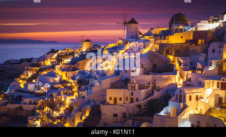 Farbenfroher Sonnenuntergang mit den Lichtern der Stadt in Oia, Santorini, Griechenland Stockfoto