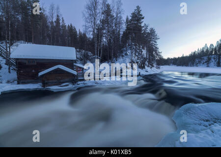 Eine Holzhütte, umgeben von den Stromschnellen und verschneite Wälder bei Abenddämmerung Juuma Myllykoski Lappland Region Finnland Europa Stockfoto