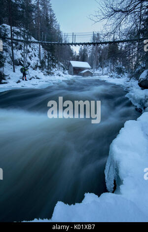 Eine Holzhütte, umgeben von den Stromschnellen und verschneite Wälder bei Abenddämmerung Juuma Myllykoski Lappland Region Finnland Europa Stockfoto