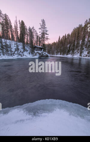 Eine Holzhütte, umgeben von den zugefrorenen Fluss und verschneite Wälder bei Abenddämmerung Juuma Myllykoski Lappland Region Finnland Europa Stockfoto