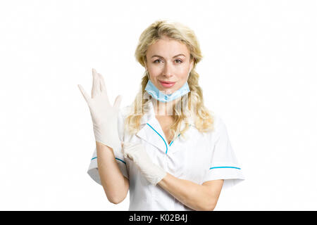 Zuversichtlich junge Krankenschwester auf Handschuhe. Schöne blonde Dame medic mit Gesichtsmaske auf weiße sterile Handschuhe auf weißem Hintergrund. Stockfoto