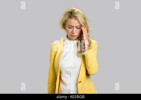 Attraktive europäische Frau mit Kopfschmerzen. Portrait von depressiven junge blonde Frau mit schreckliche Kopfschmerzen berühren Tempel über grauen Hintergrund. Stockfoto