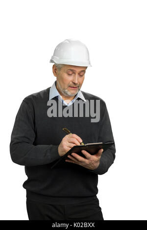 Zuversichtlich reife Supervisor schreiben auf Zwischenablage. Älterer Mann im weißen Helm Schrift auf schwarzen Zwischenablage, weißen Hintergrund. Stockfoto